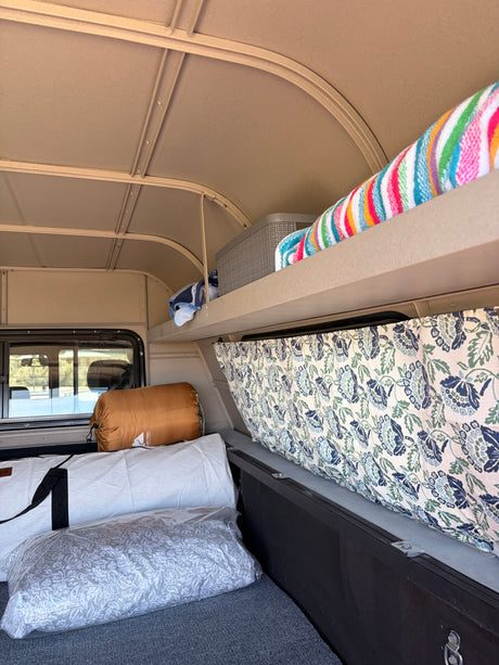 RV rental camper interior showcasing an organized sleeping area, patterned curtains, and convenient overhead storage.