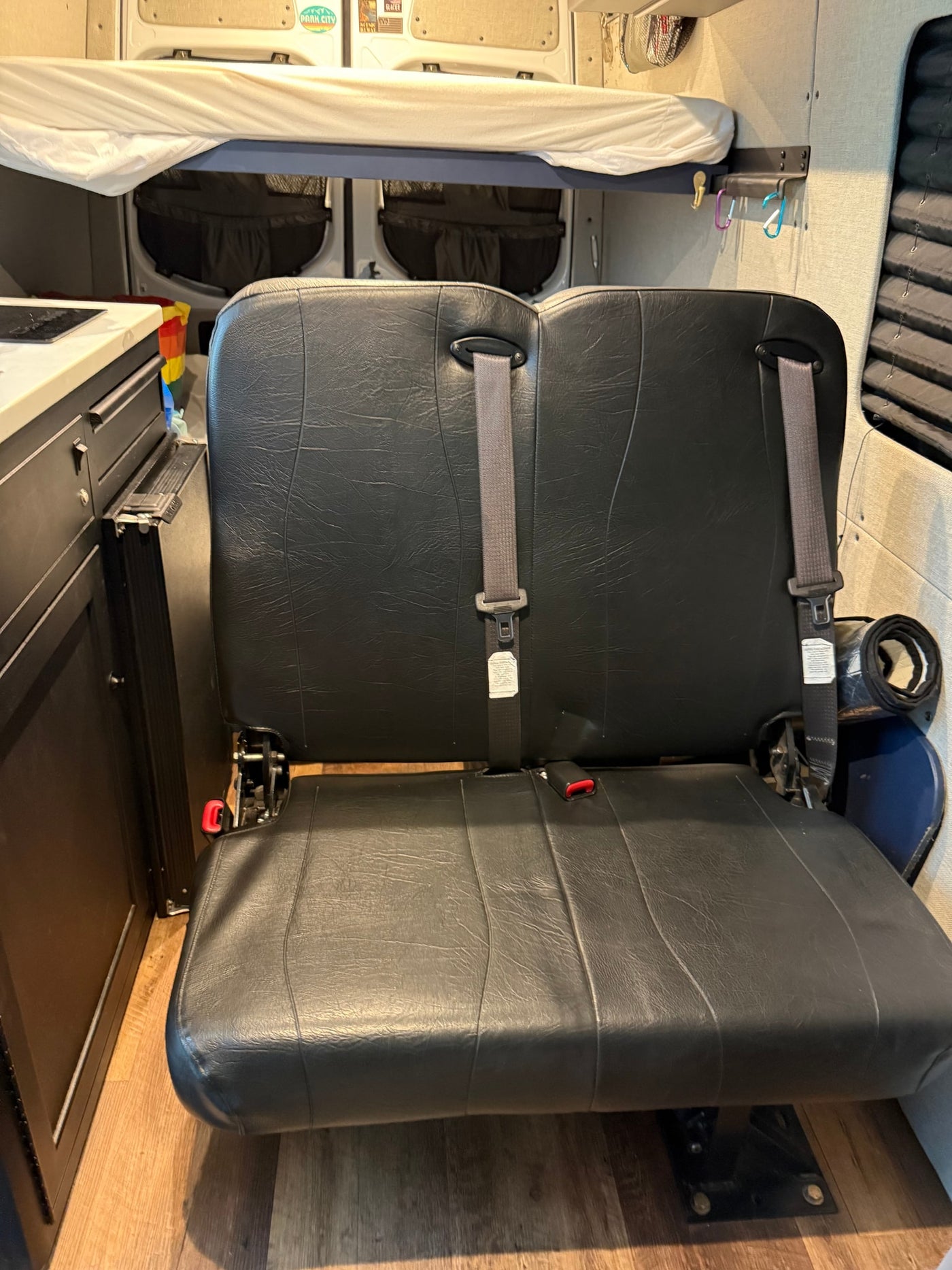 Compact RV rental interior featuring a convertible bench seat with seatbelts, overhead bunk bed, and kitchenette. — photo 16