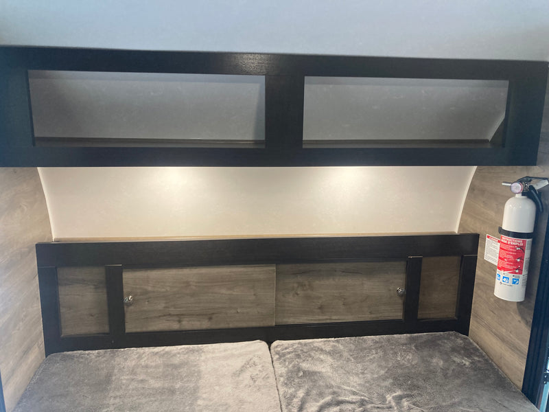 This RV rental features a comfortable bed, convenient overhead storage cabinets, and essential safety equipment like a fire extinguisher. — photo 6