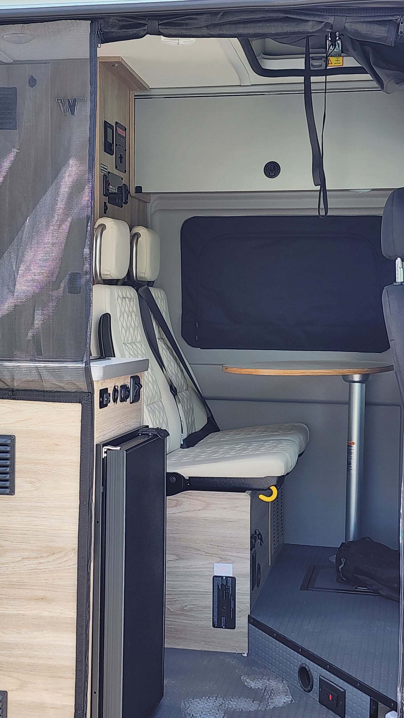 RV rental interior: view of a convertible bed/seating area, controls, and storage space in a compact camper van.