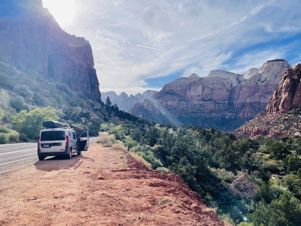  overlooking a river bordered by striking red rock canyons.|Scenic RV rental adventure in Zion National Park: a camper van pauses on red dirt — photo 4