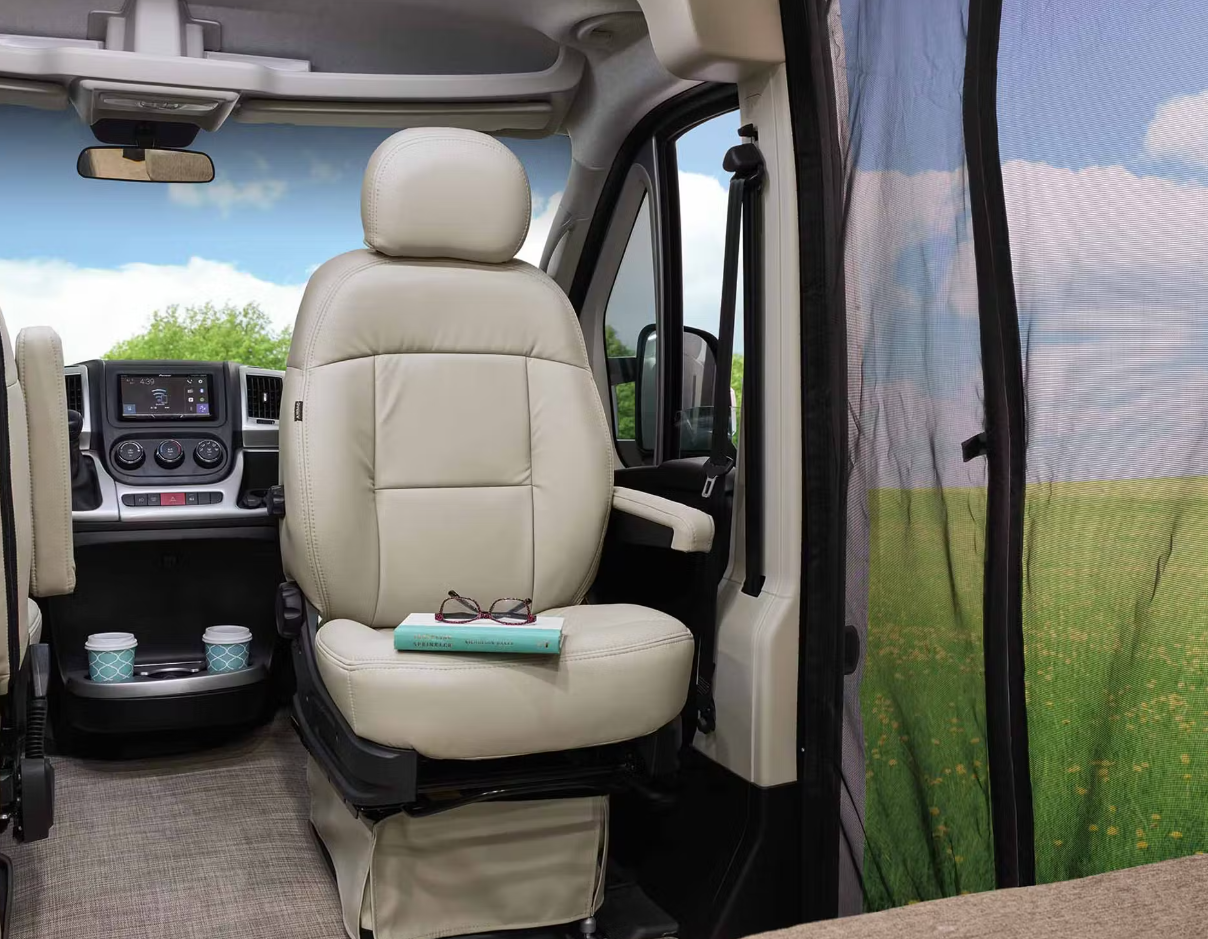 Cream swiveling front seat with a book, modern dash, and mesh door in this spacious RV rental interior. — photo 12