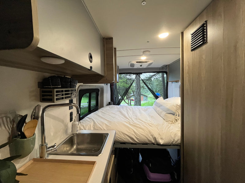 Cozy RV rental interior features a spacious bed, functional sink area, and scenic forest views from the rear window. — photo 4