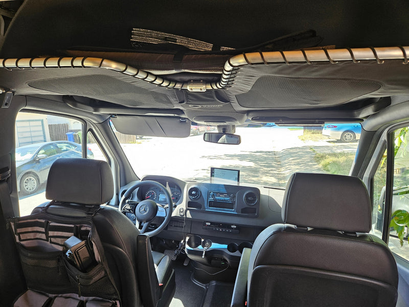 Inside a Mercedes Sprinter RV rental. Front cabin view with steering wheel, dashboard, and custom mesh overhead storage. — photo 6