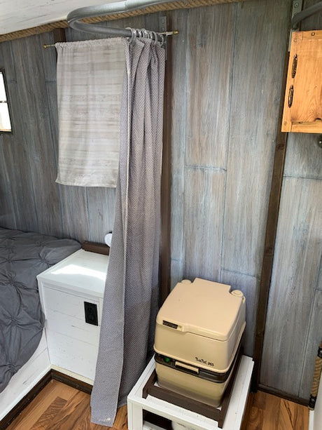 Inside your RV rental: a compact layout with a portable toilet, privacy curtain, and cozy bed.