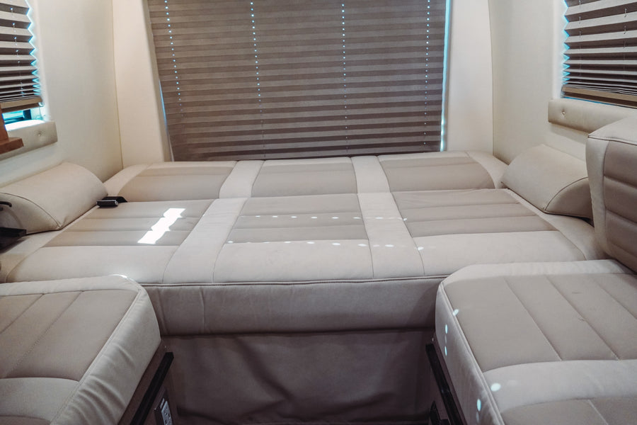 This RV rental features a light-colored, upholstered seating area configured as a bed, with horizontal window blinds.