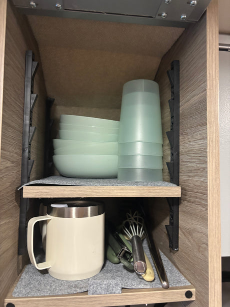 RV rental kitchen cabinet: neatly organized bowls, cups, and utensils on felt-lined shelves, perfect for compact living.