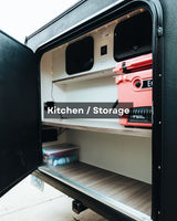 An open RV rental exterior compartment with shelves, a pink cooler, and organized supplies for an outdoor kitchen/storage setup.