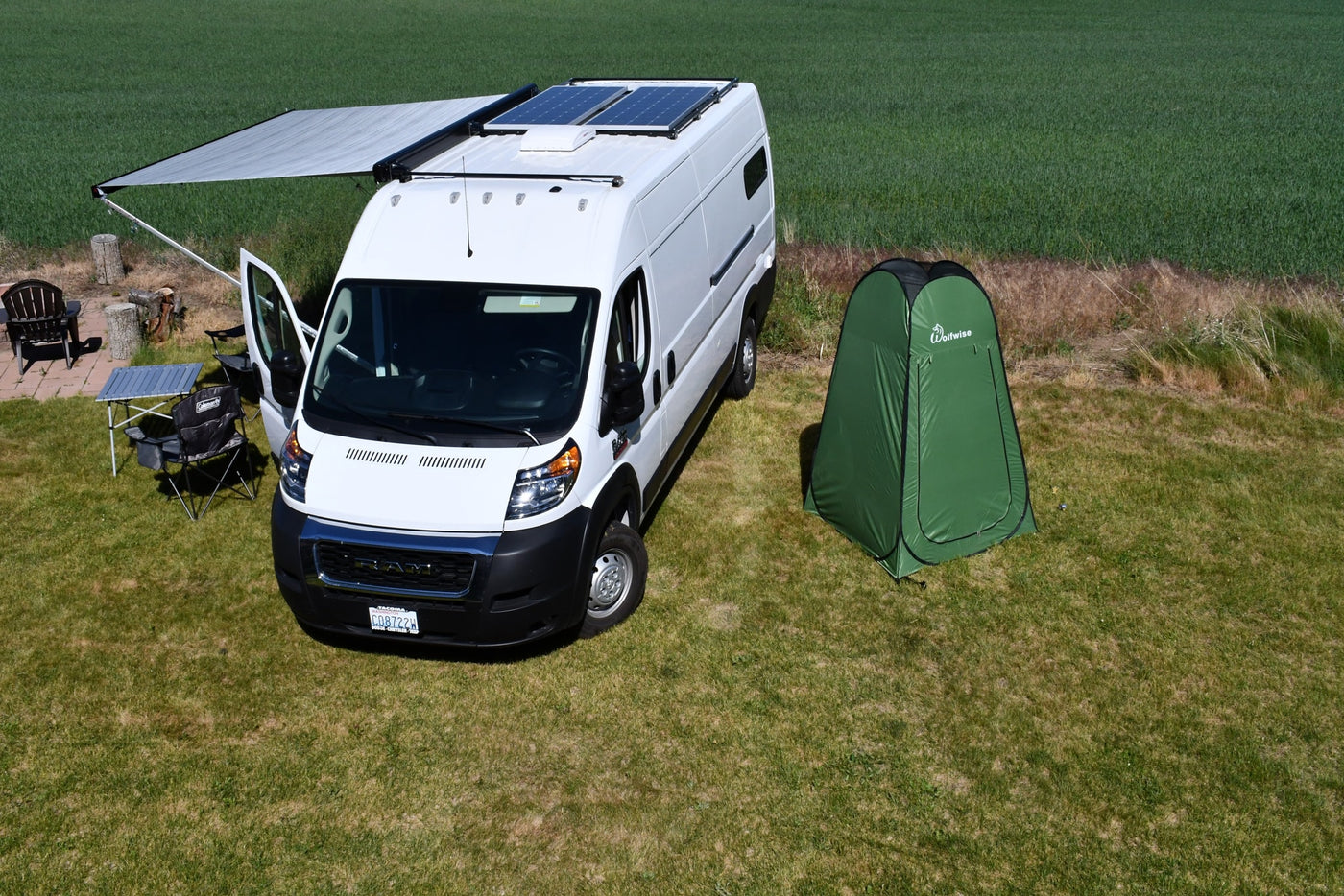 An rv rental white camper van with solar panels, extended awning, and a green privacy tent set up on a sunny grassy field. — photo 20