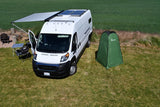 An rv rental white camper van with solar panels, extended awning, and a green privacy tent set up on a sunny grassy field.