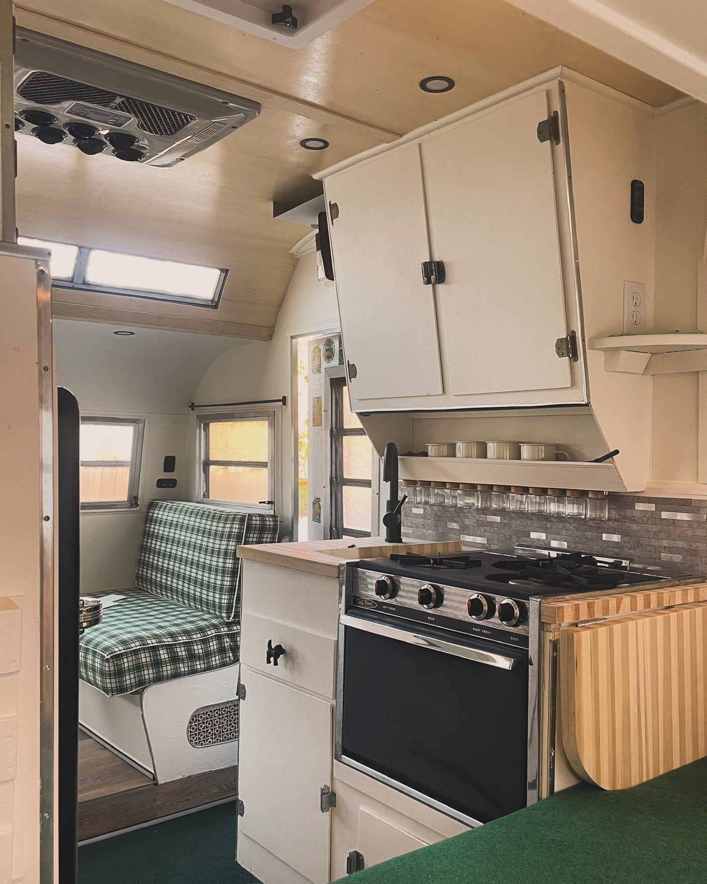 Cozy RV rental kitchen & dining area, featuring a modern gas range, sink, and charming plaid dinette. Ready for adventures!