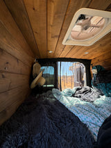 Inside an rv rental: rustic wooden interior, comfy bed, and mesh windows revealing a sunny desert landscape.