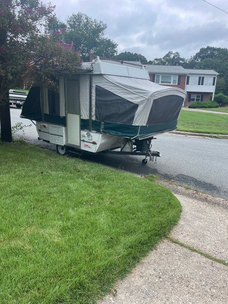 A Coleman Taos pop-up camper, an excellent RV rental option, parked on a grassy verge by a residential street.