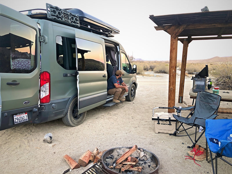 A man relaxes in his green RV rental camper van at a desert campsite, ready for a campfire and outdoor cooking. — photo 10