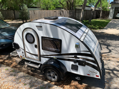 White T@G teardrop trailer with black stripes and solar panels, perfect for an RV rental adventure, parked outside.