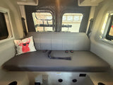 RV rental: Rear seating area of a comfy camper van, featuring a plush bench, safety belts, and a fun deer pillow.