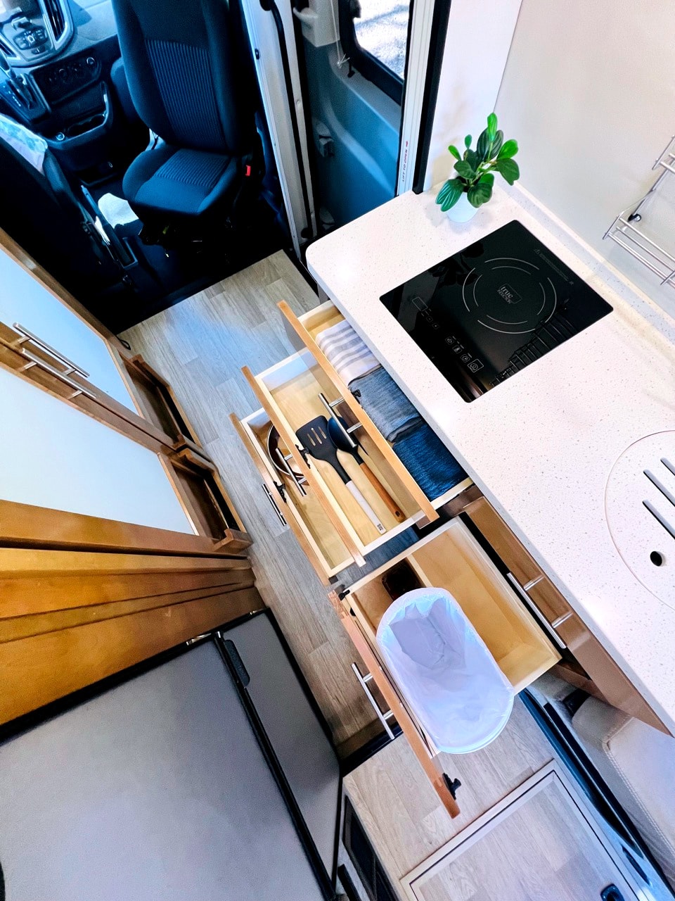 Inside an RV rental: a modern kitchen with an induction stove, organized drawers for utensils & towels, plus a hidden trash bin. — photo 10