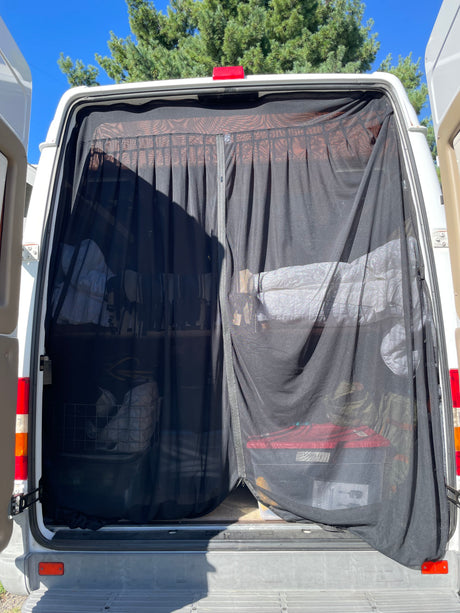 Rear view of an RV rental van with a black mesh bug screen covering the open back, revealing organized interior storage.