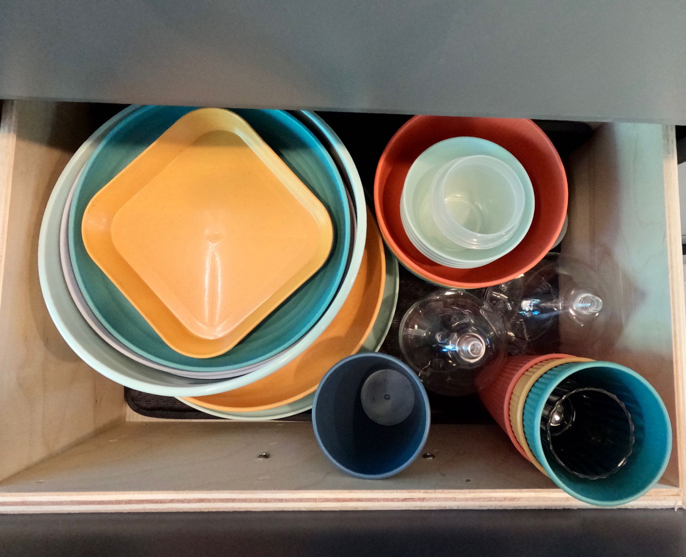 Colorful plastic plates, bowls, cups, & glasses neatly stored in an RV rental drawer.
