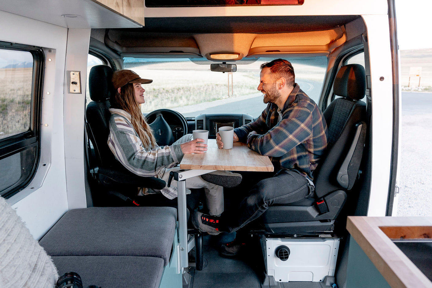 Couple enjoying coffee at a table in their RV rental. Ideal for a comfortable road trip adventure.