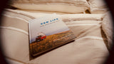 A "Van Life" book featuring a red camper van rests on cozy, striped bedding. Perfect for planning your next rv rental adventure.