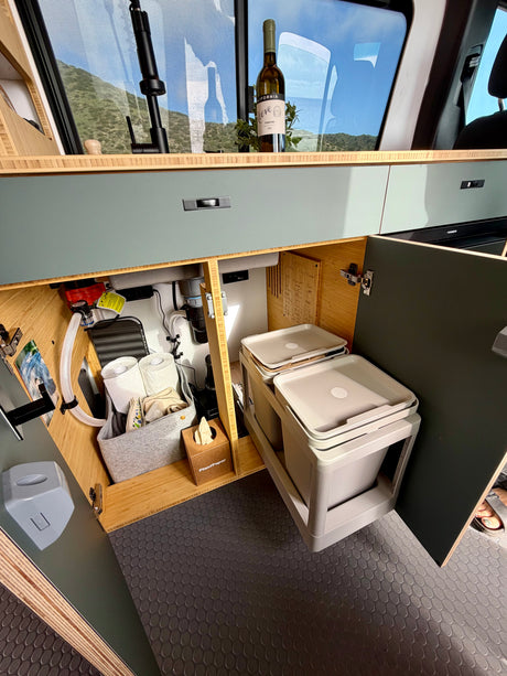 Organized RV rental kitchen interior featuring under-sink storage, pull-out bins for waste, & a scenic mountain view.