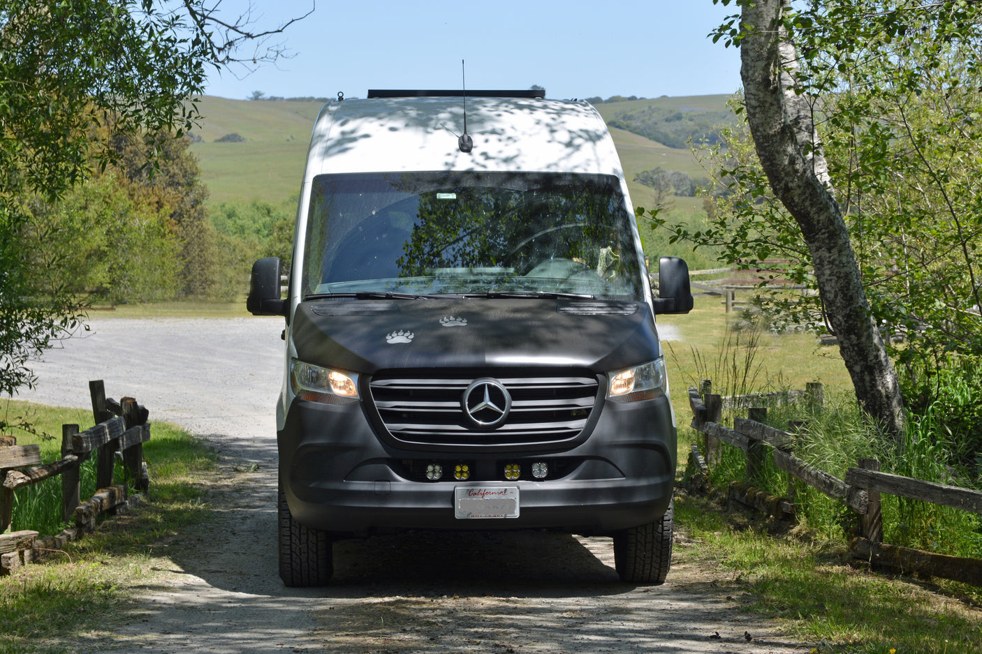 Camper van RV rental on a gravel road, surrounded by trees & hills. Perfect for exploring nature.