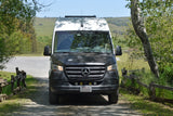 Camper van RV rental on a gravel road, surrounded by trees & hills. Perfect for exploring nature.