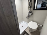 RV rental's compact bathroom showing a white shower stall, toilet, and tied-back geometric shower curtain.