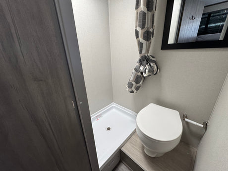 RV rental's compact bathroom showing a white shower stall, toilet, and tied-back geometric shower curtain.