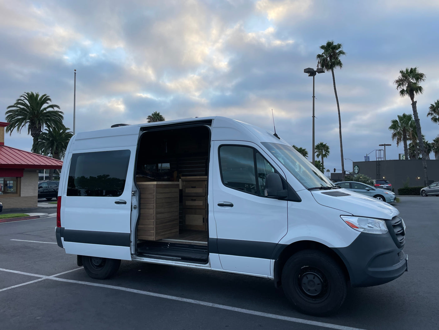 White Mercedes Sprinter RV rental van parked, its side door open to reveal a custom wooden interior.