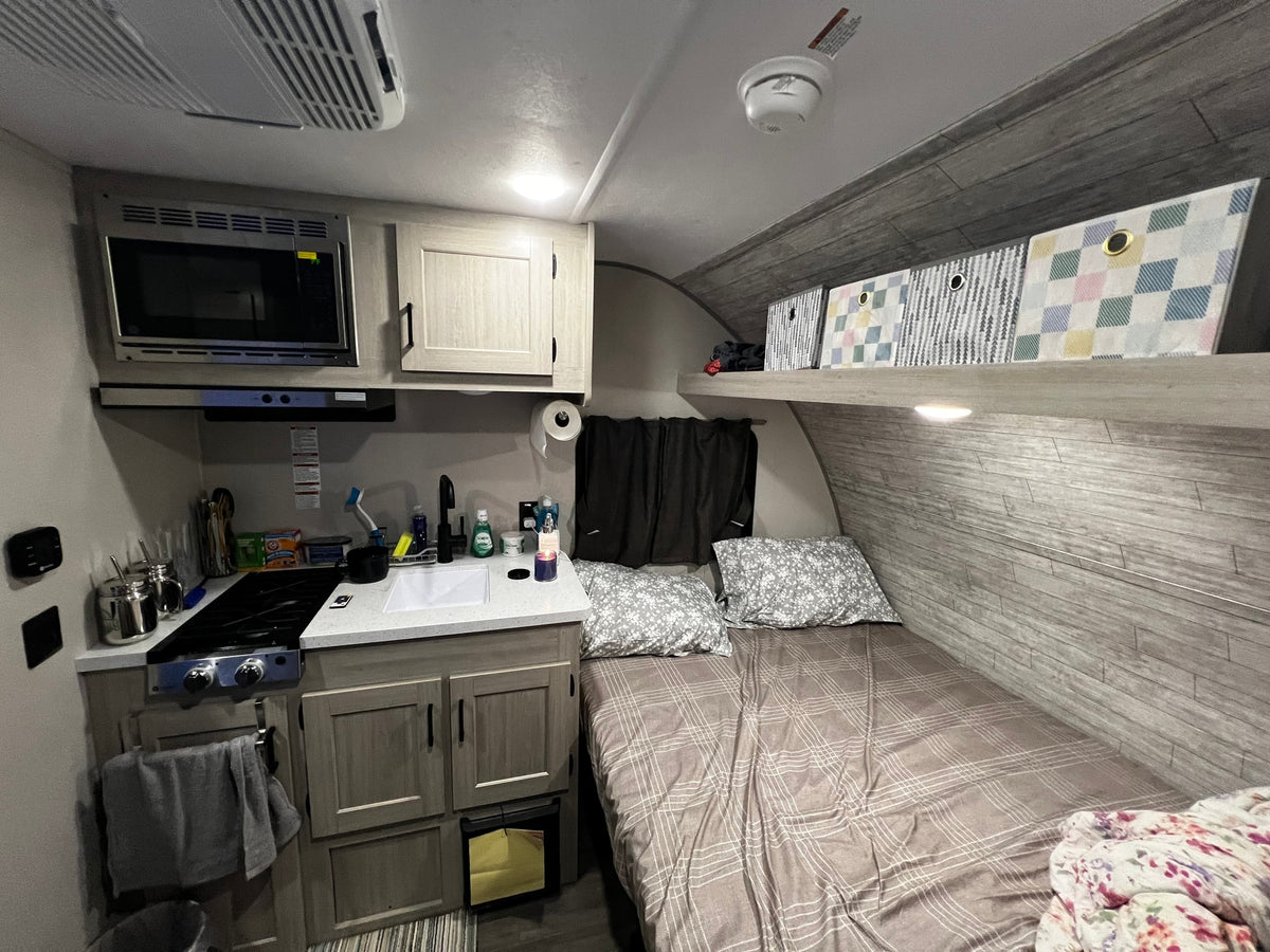 Compact rv rental interior featuring kitchen with microwave, stove, sink, and a comfortable bed with patterned bedding and storage. — photo 7