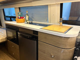 RV rental kitchen featuring a compact counter, sink, stovetop, microwave, and fridge, integrated into modern wood-look cabinetry.