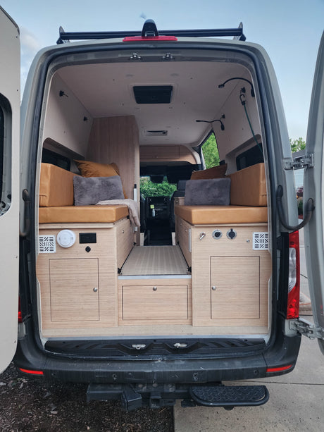 Detailed rear view of a custom RV rental van interior, featuring built-in wood cabinetry, cozy bed platforms, and storage solutions.