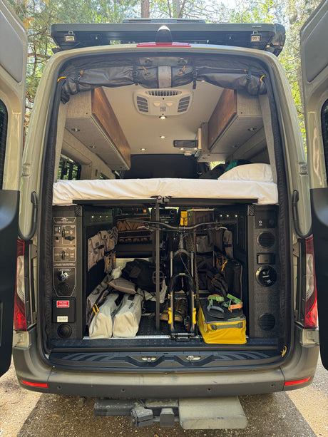 Adventure-ready RV rental: rear view of a camper van's smart gear storage, bike rack, and raised bed.
