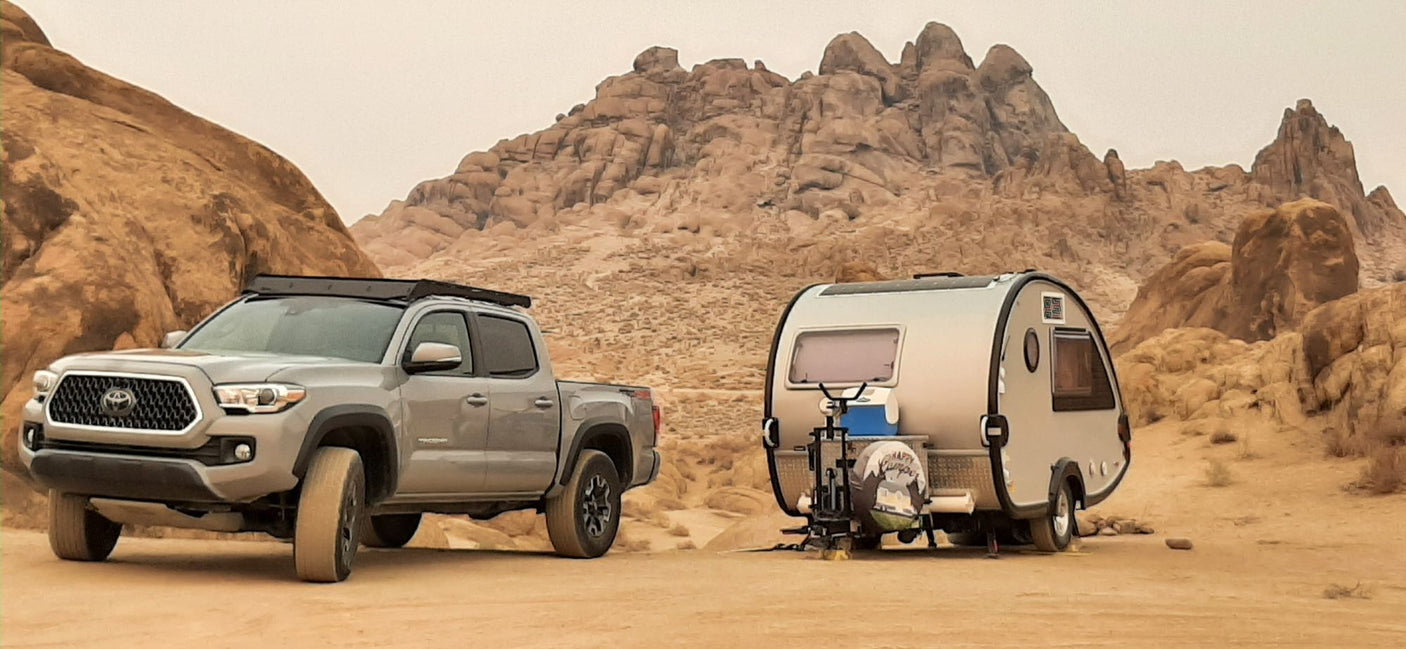 Off-road adventure: Grey Toyota truck and compact RV rental parked in rocky desert.