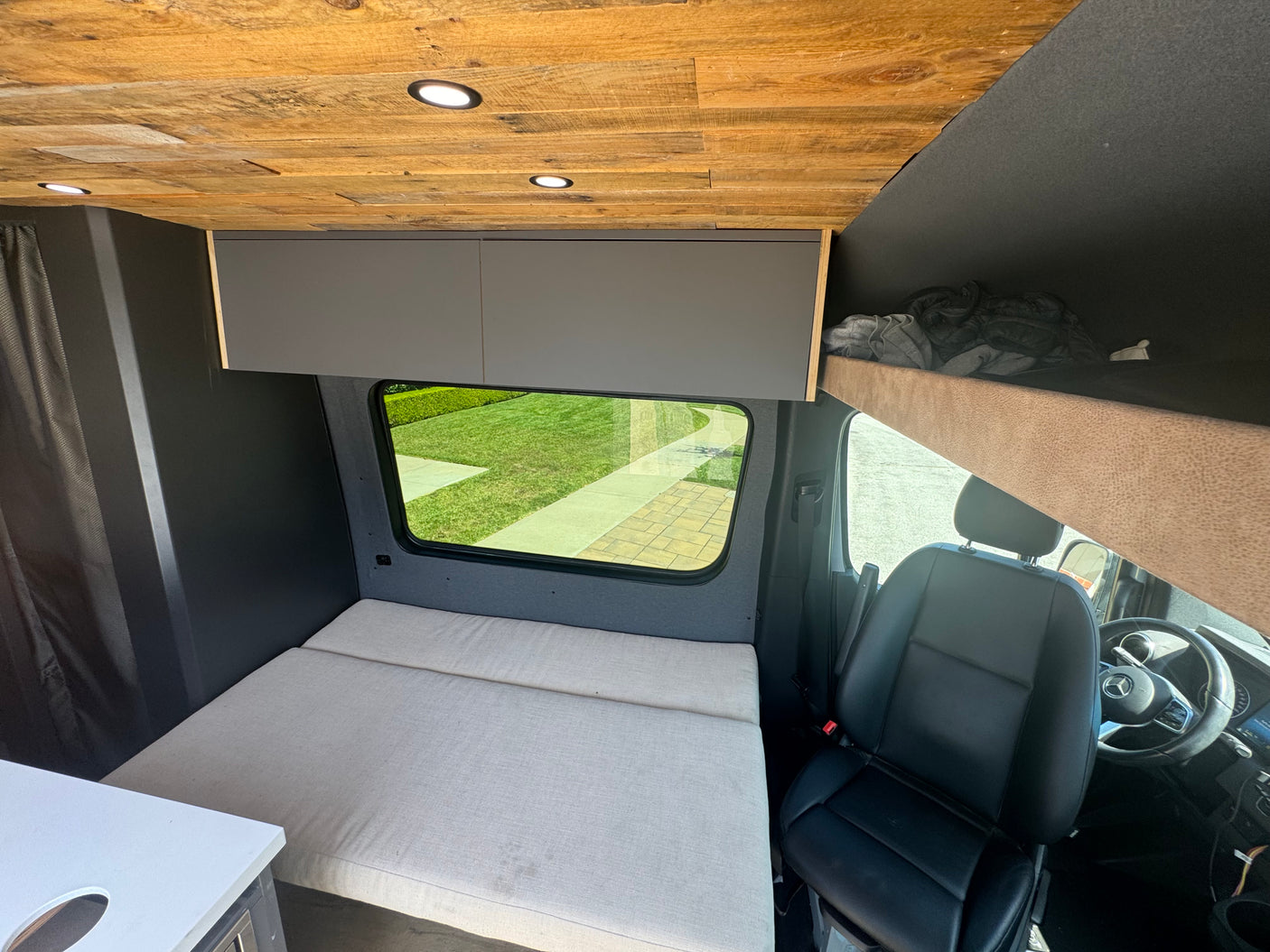 Compact rv rental interior featuring a wooden ceiling, cozy bed, overhead cabinets, and driver's area, ideal for travel.