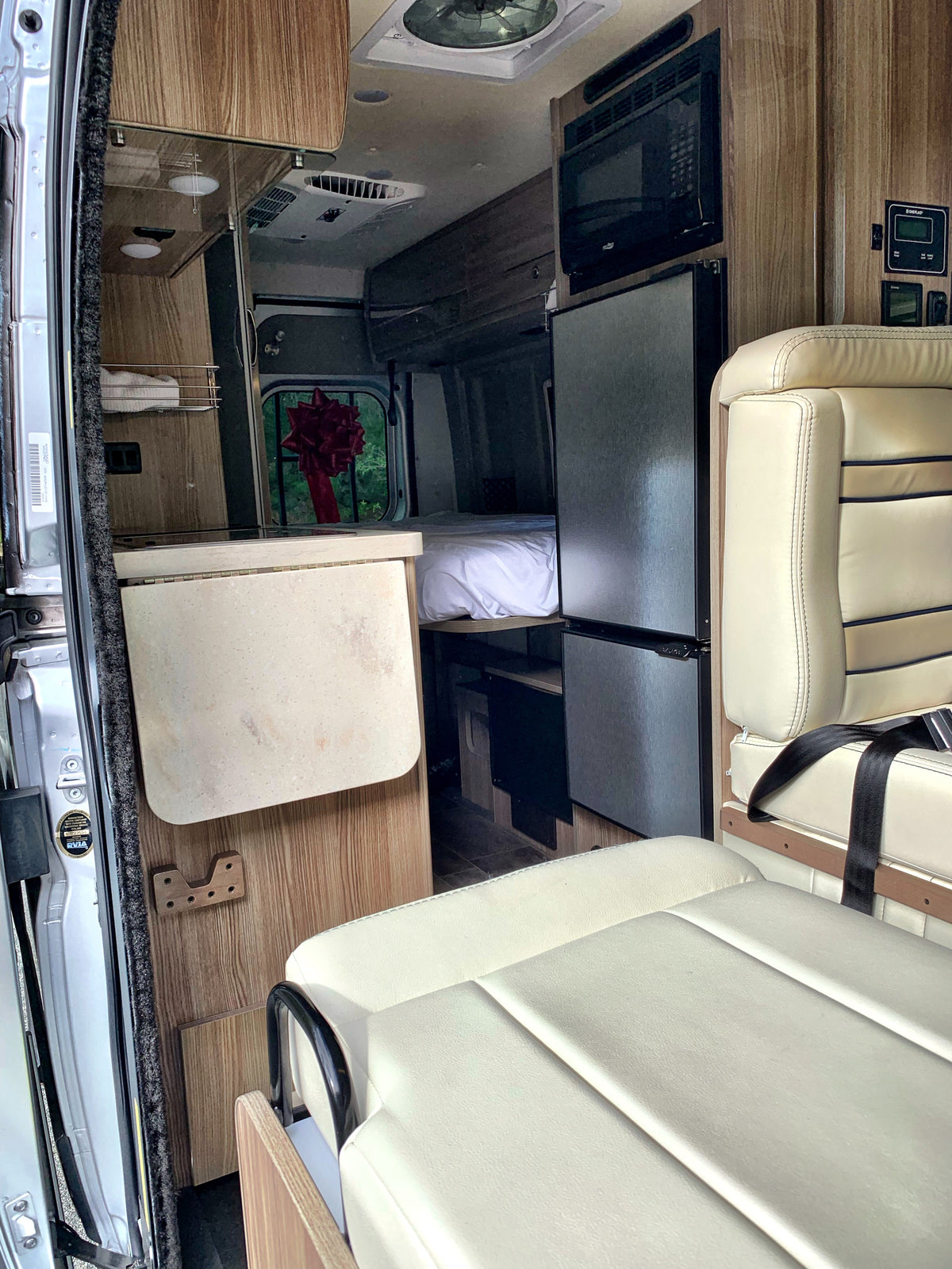 This RV rental interior showcases a compact kitchen with microwave, fridge, and comfortable seating and bed areas.