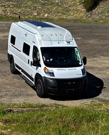 An rv rental white camper van with solar panels on its roof, parked on a dirt road for outdoor adventure.