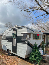 Charming vintage Comet travel trailer, adorned with holiday decor & string lights. Ideal RV rental for festive adventures!