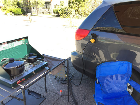 RV rental cooking setup: Van with shore power, Coleman stove, and chair for outdoor meals.