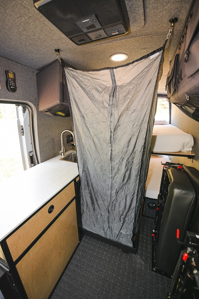 RV rental interior with kitchen sink, deployable privacy curtain, and rear bunk beds.