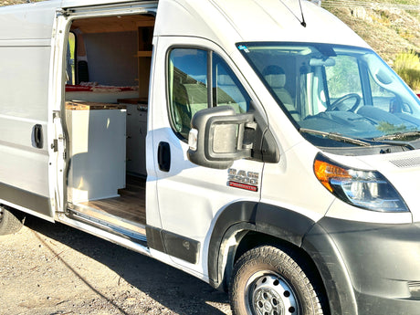 White Ram ProMaster camper van with side door open, revealing custom interior. Explore in style with this RV rental.
