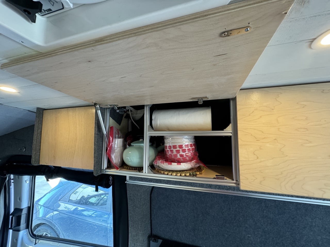 Organized overhead storage in an RV rental, showcasing custom wooden cabinets, a teapot, and dishes, ideal for van life travel.