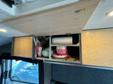 Organized overhead storage in an RV rental, showcasing custom wooden cabinets, a teapot, and dishes, ideal for van life travel.