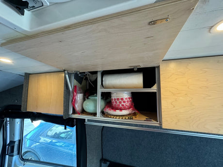 Organized overhead storage in an RV rental, showcasing custom wooden cabinets, a teapot, and dishes, ideal for van life travel.