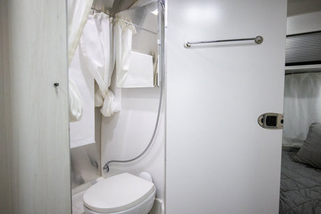 Clean rv rental interior featuring a compact shower and toilet area, with a glimpse of the comfortable bedroom.