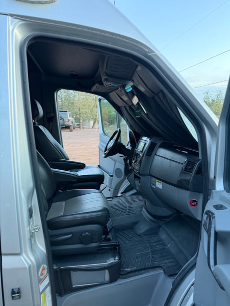 Spacious rv rental cab with black leather seats, dashboard, and steering wheel, viewed from the open driver's door.