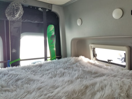 Cozy RV rental interior featuring a fluffy white bed, skis, and a window, ideal for winter sports adventures.