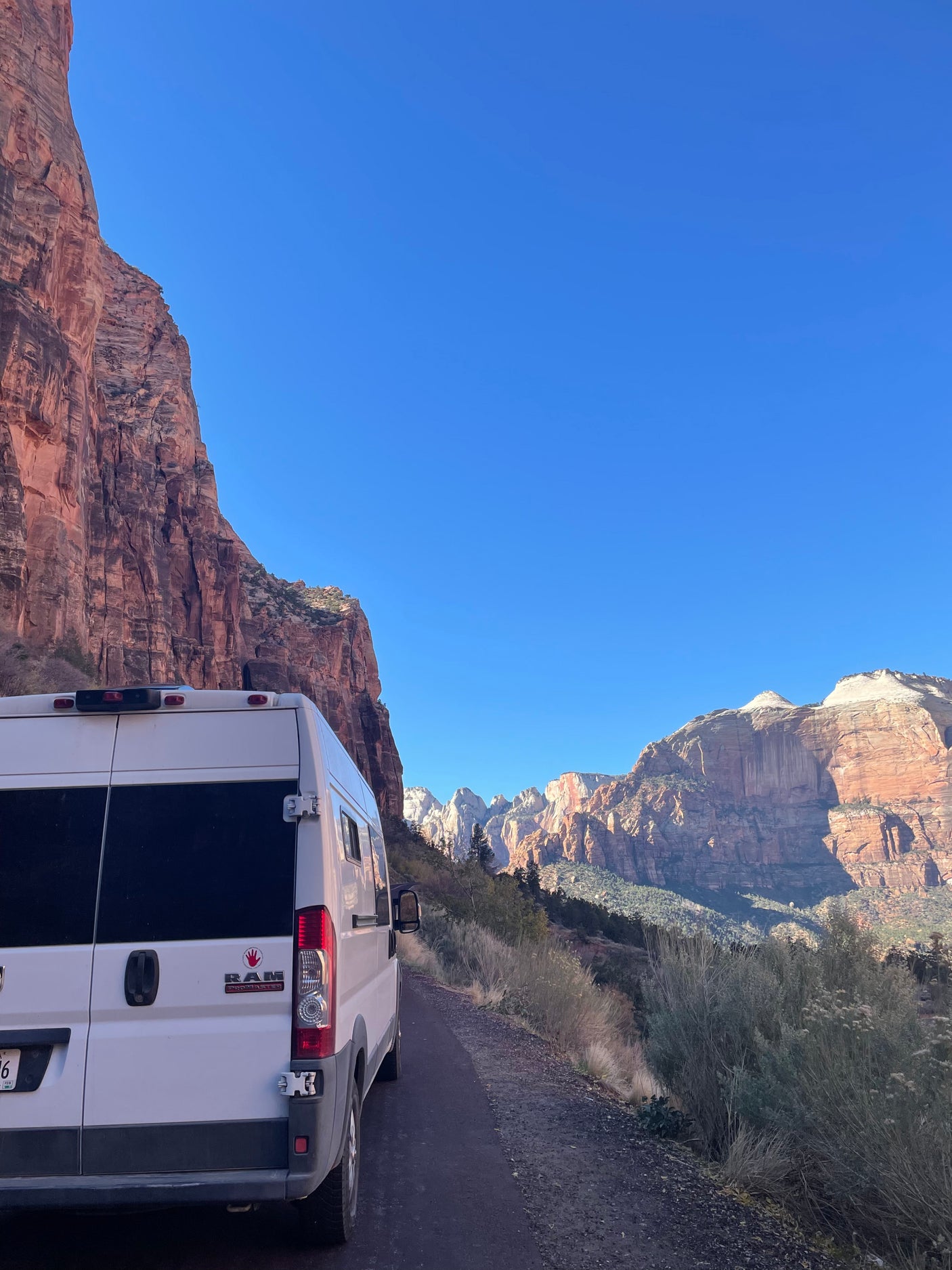 White RV rental on a dirt road, backed by majestic red rock mountains under a clear blue sky. A travel adventure.